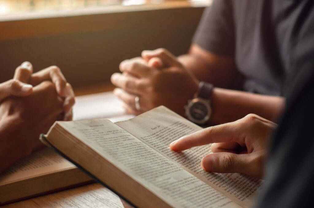 young man reading bible with friends who are praying to God Join the cell group at the church.